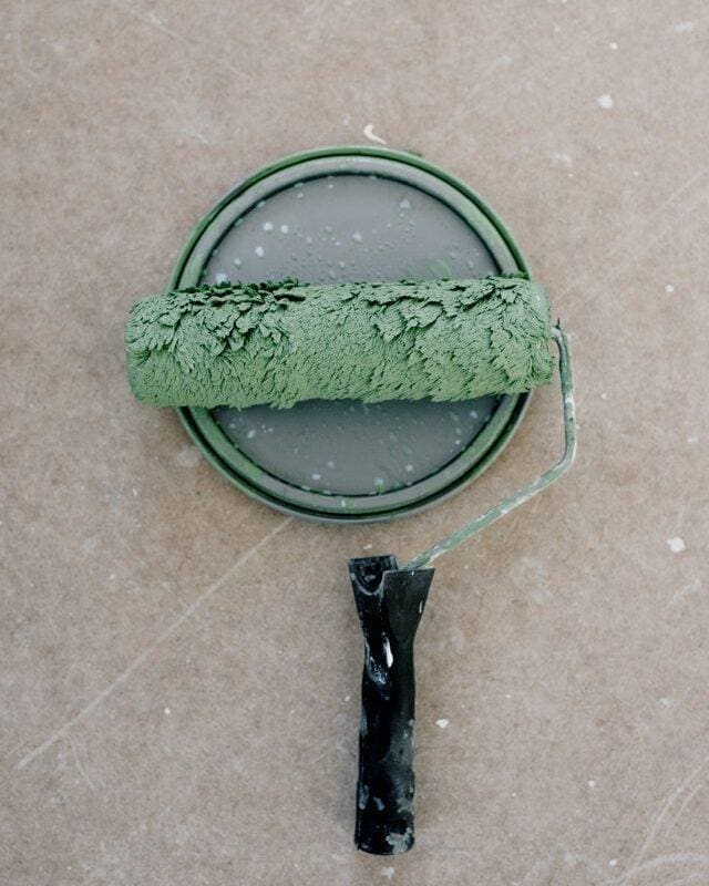 A paint brush dipped into green colour during wall maintenance.